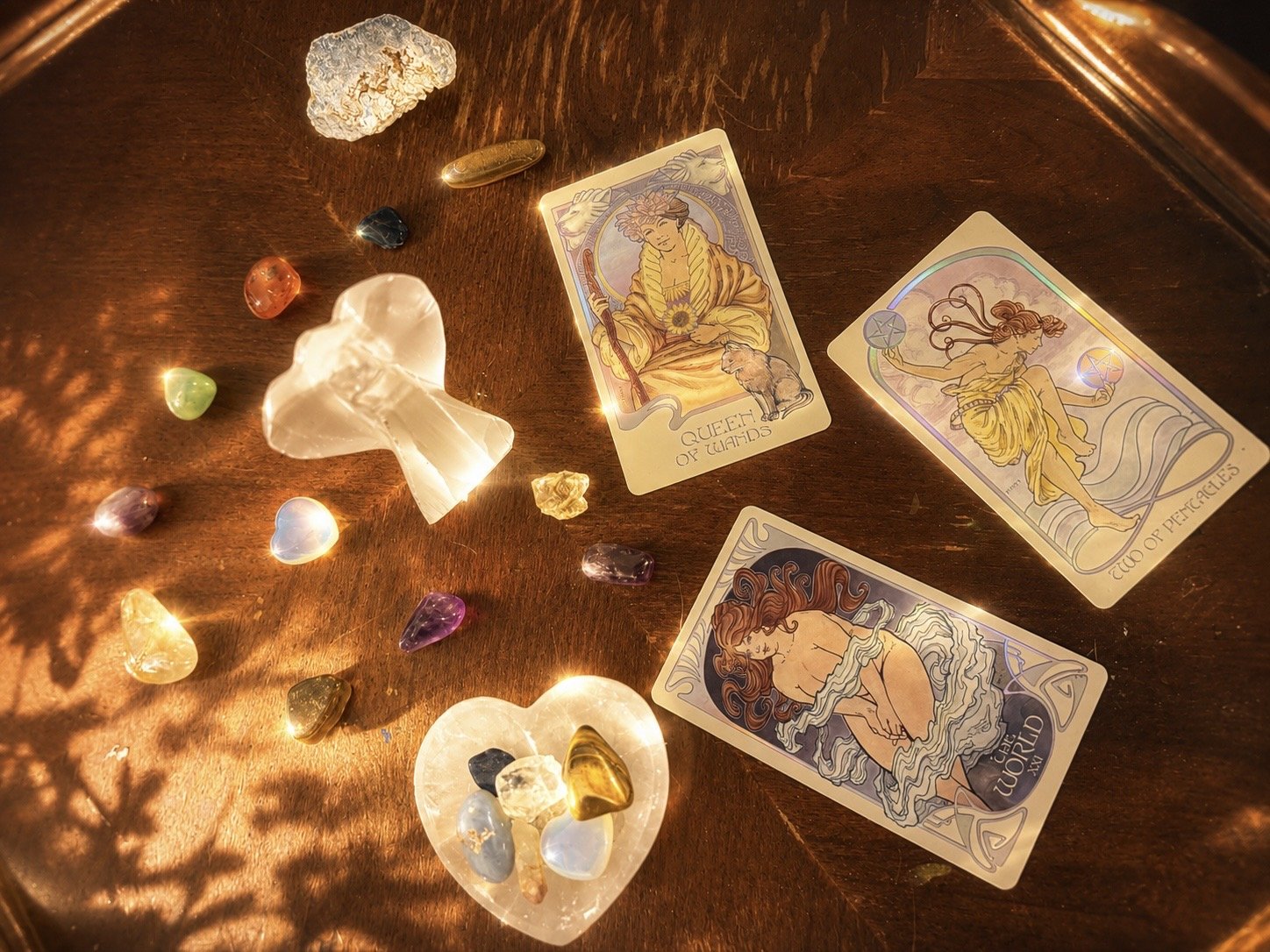 Tarot cards, colorful gemstones, and crystal fragments on a wooden surface illuminated by warm light.