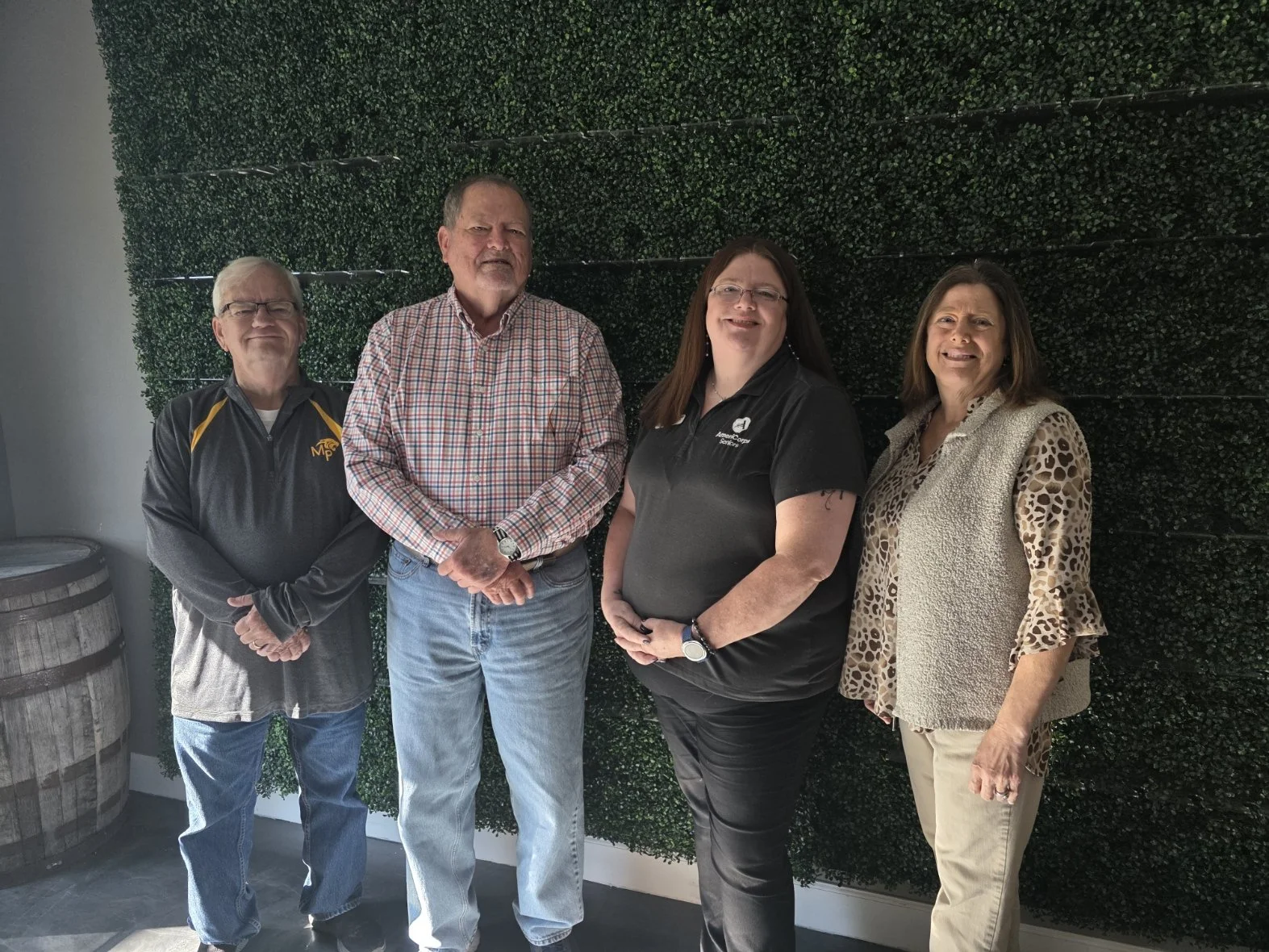 Four people standing in front of a green wall with a barrel and wine cask on the side.