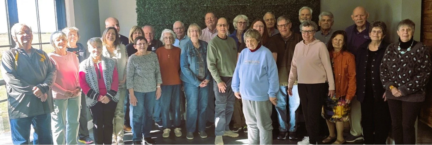 Group of elderly people gathered indoors for a photo, some smiling and others looking at the camera.
