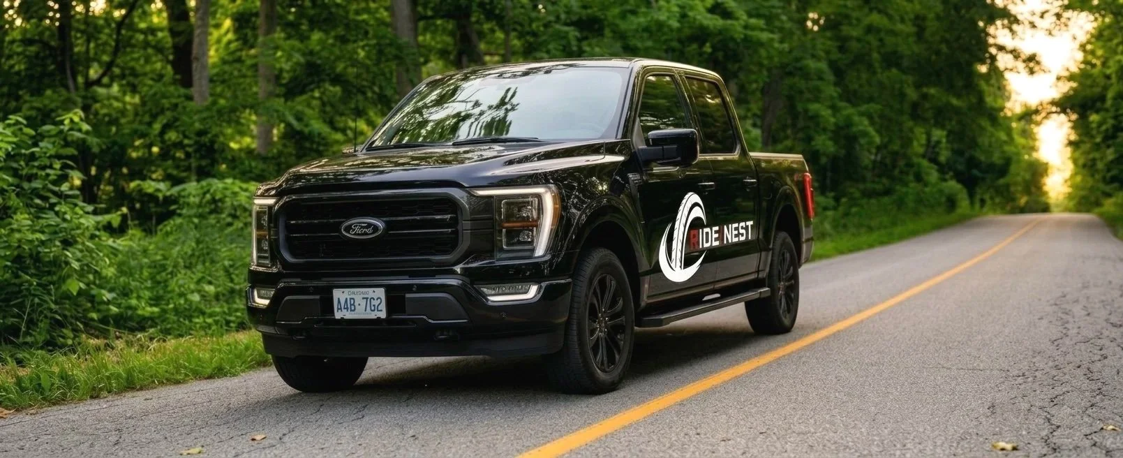 A black Ford pickup truck with a Ride NEST logo parked on a rural road surrounded by trees and greenery.