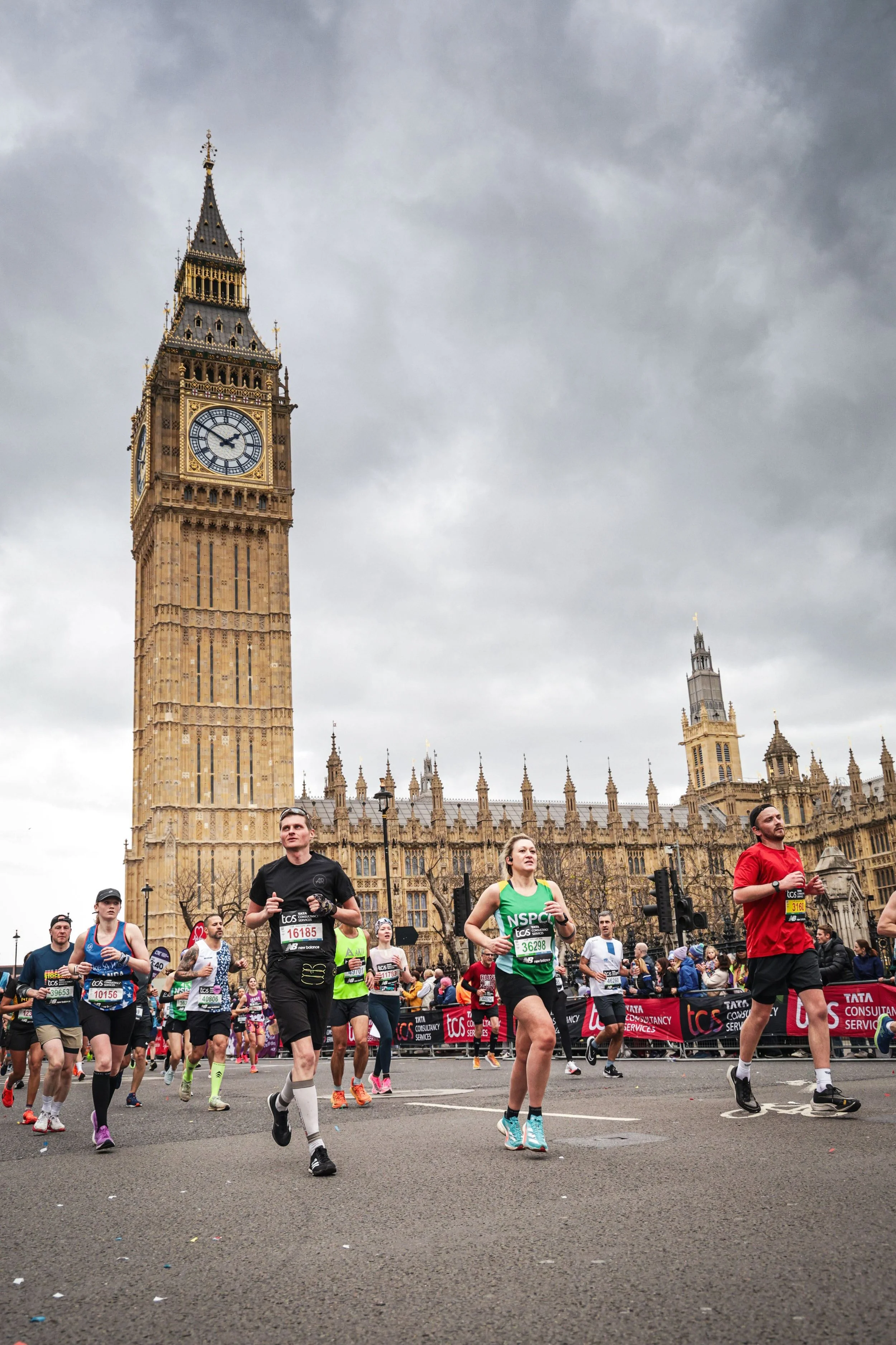 Marathon runners participating in a race near Big Ben and the Houses of Parliament in London, with cloudy skies overhead.