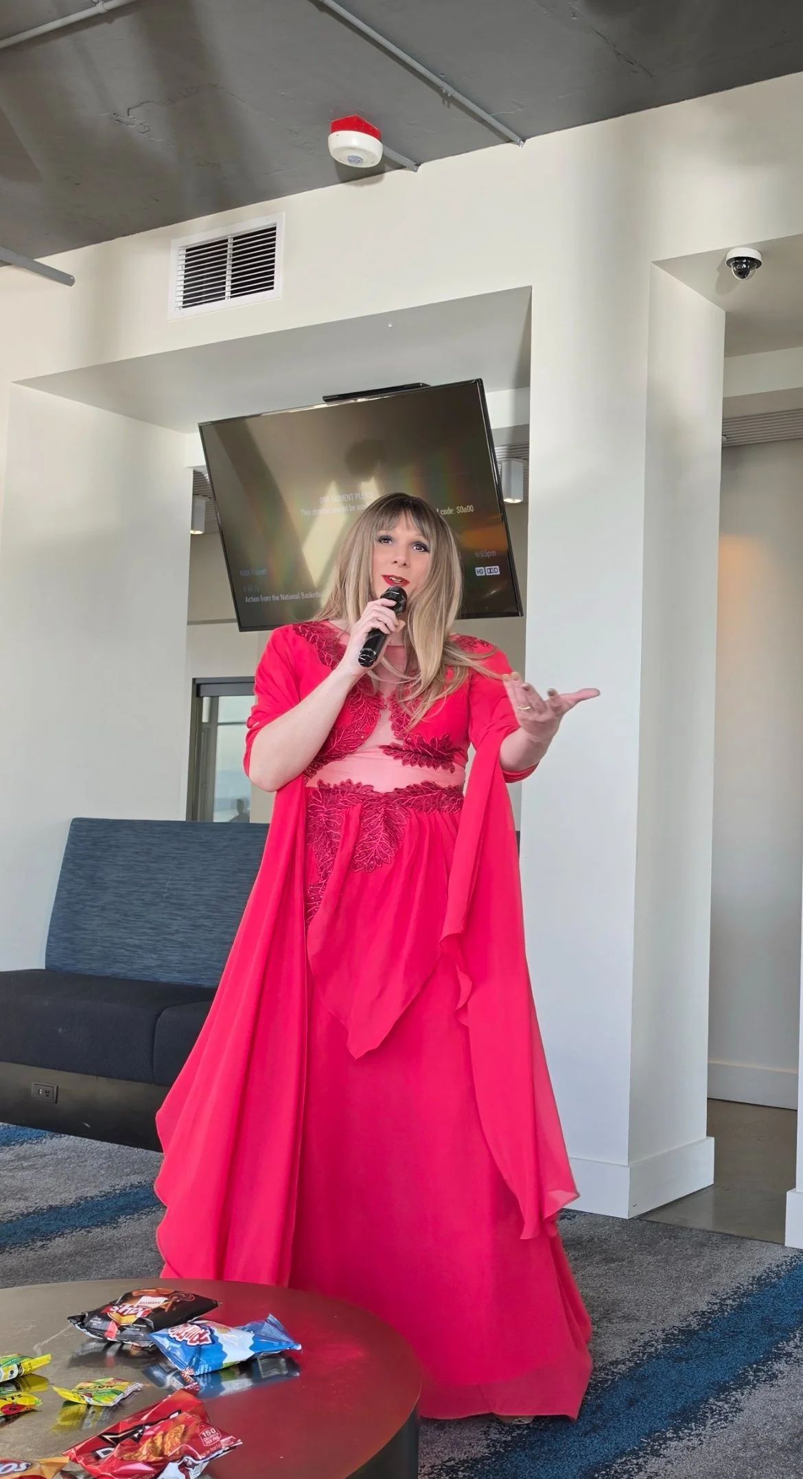 Woman in a red dress speaking into a microphone in an indoor setting.