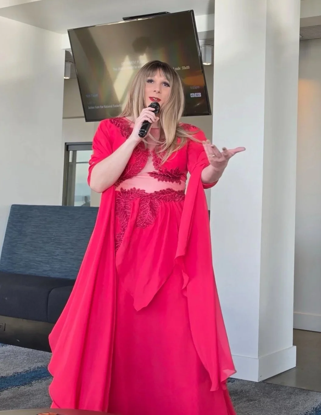 A woman in a bright pink dress speaking into a microphone in a modern indoor setting.