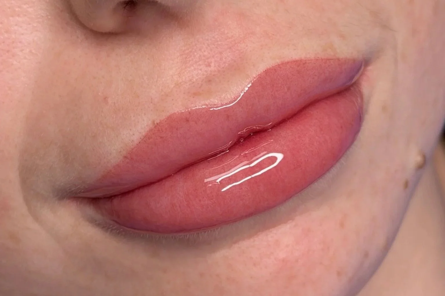 Close-up of a person's lips with gloss applied, showing smooth skin and natural lip color.
