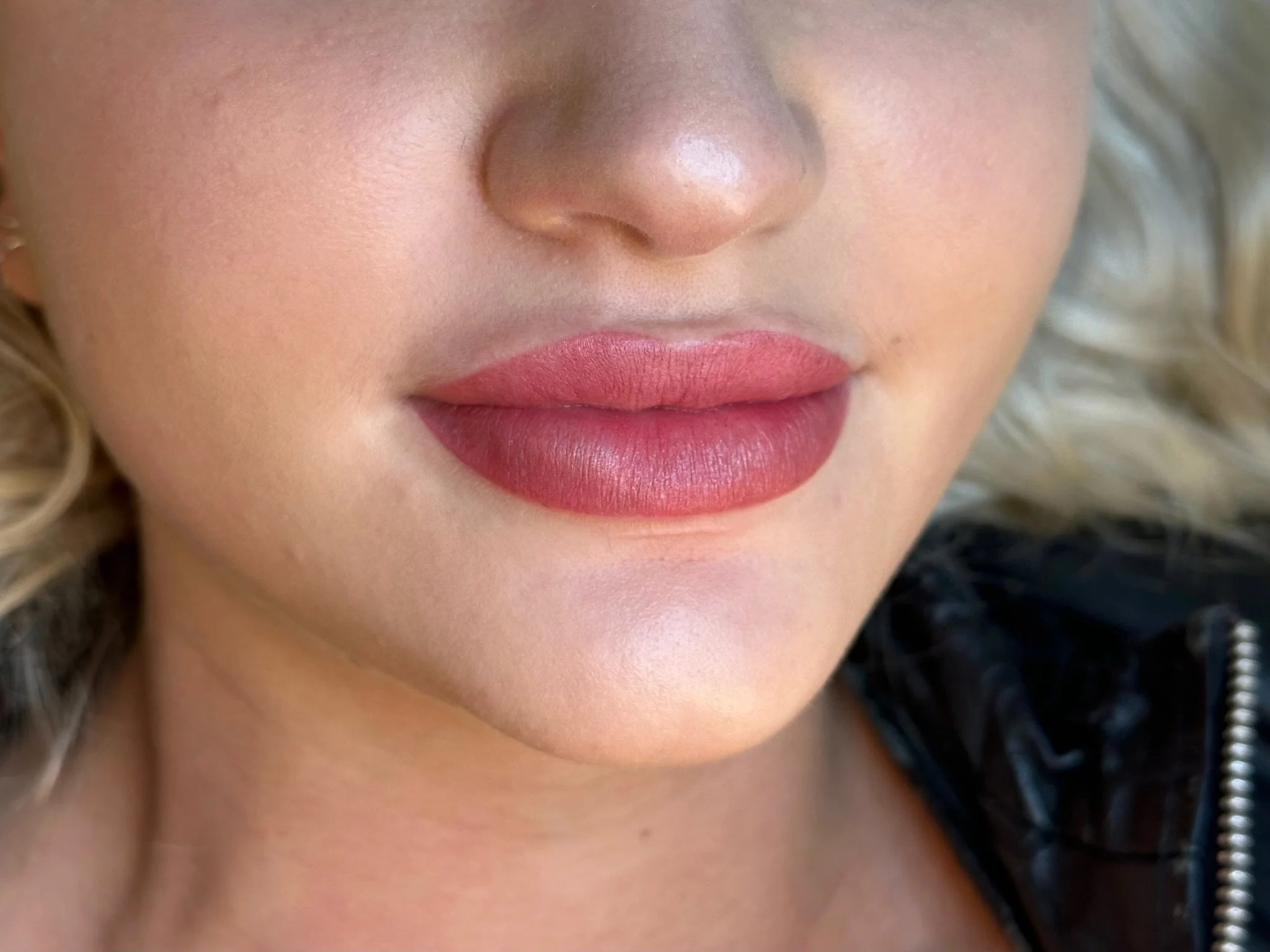 Close-up of a woman's lips with pink lipstick, her nose, and part of her cheeks visible, with blurred background.