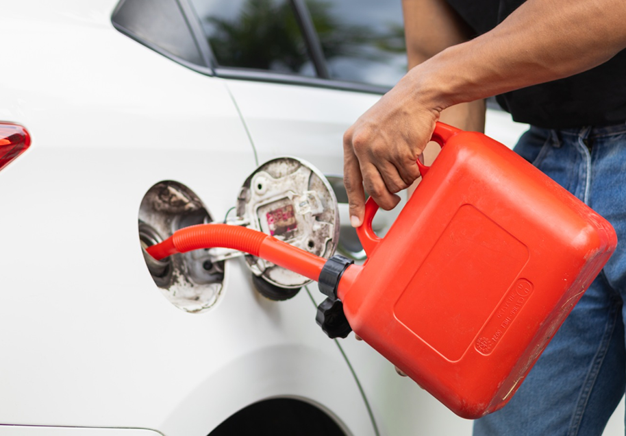 Person filling a white car with fuel using a red gas can.