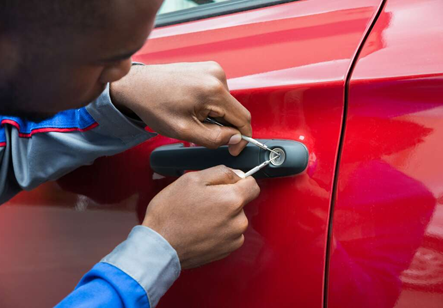 A person using a tool to unlock a red car door.