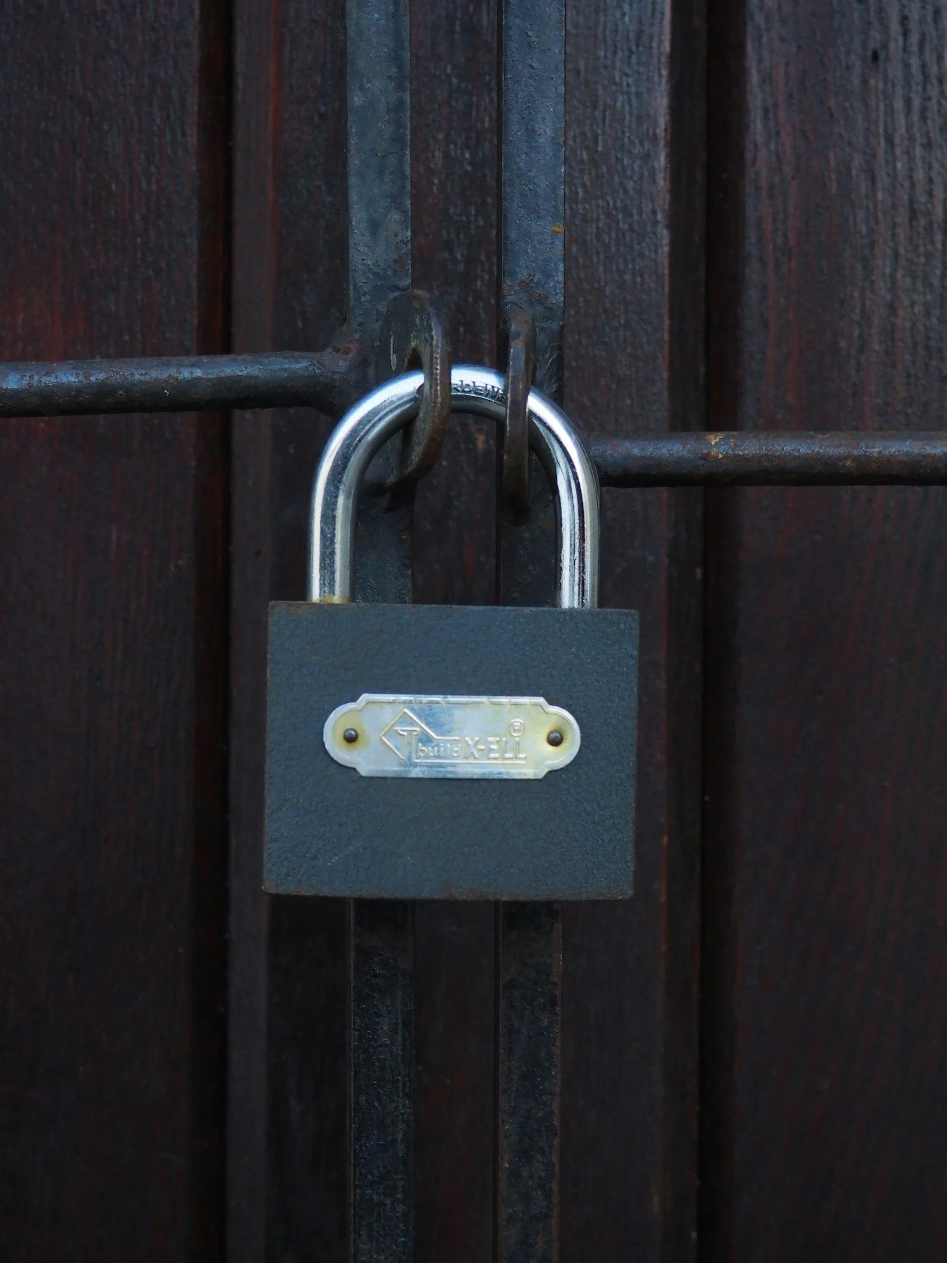 A close-up photo of a padlock securing a dark wooden gate.