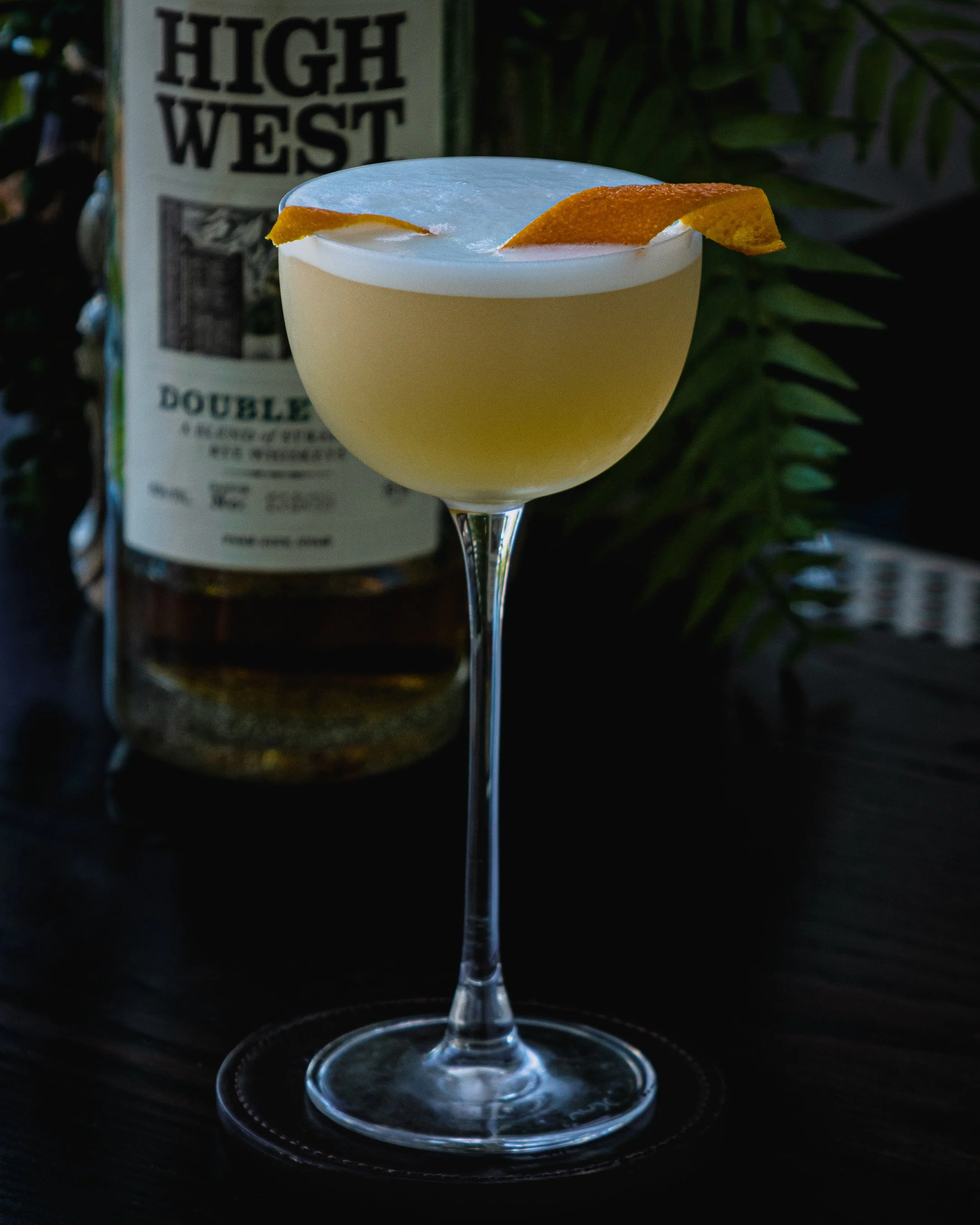 A Whiskey Sour cocktail, served in a coupe & garnished with an orange twist.
