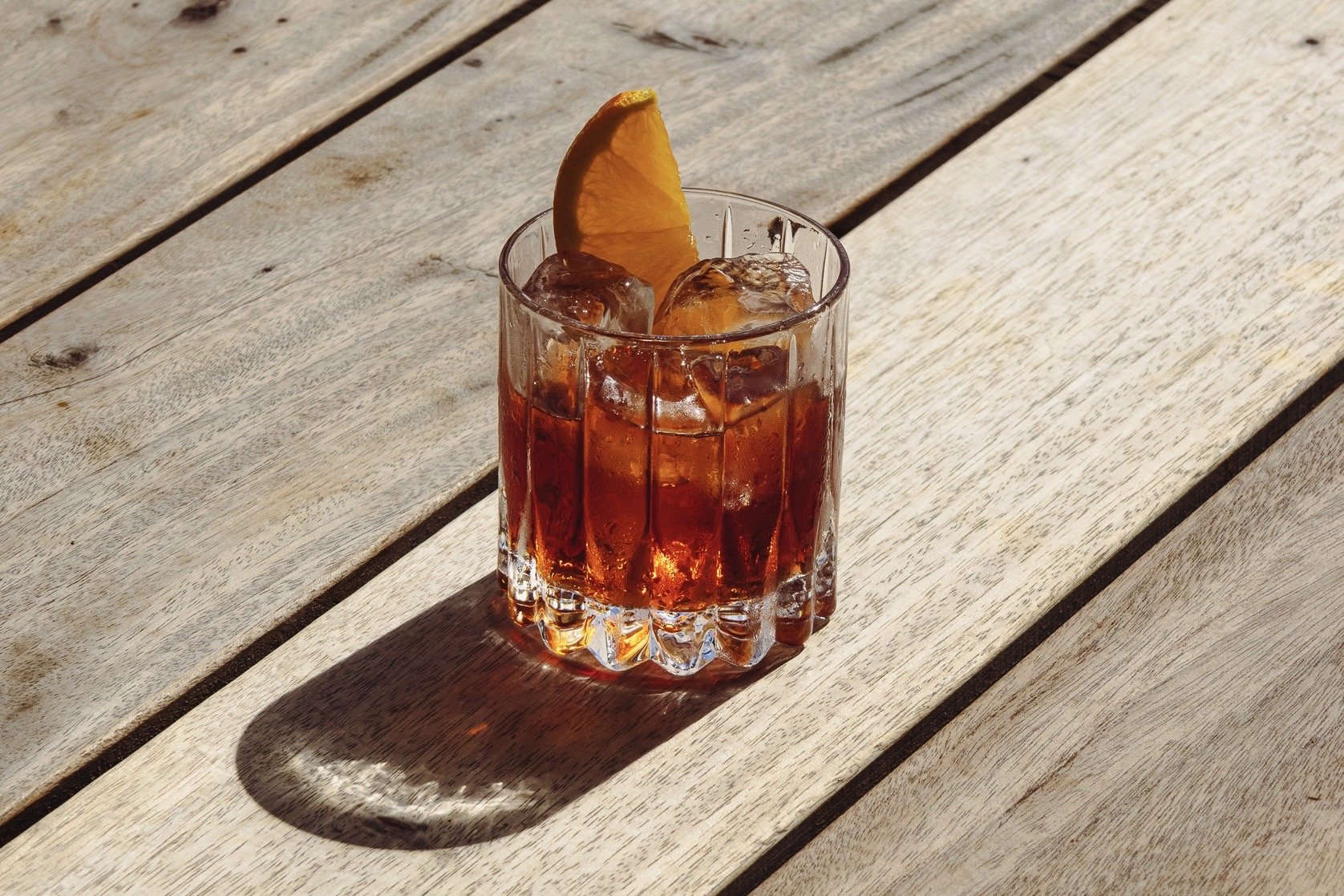 Golden hour negroni, sat on top of a textured wooden table in the afternoon sun.