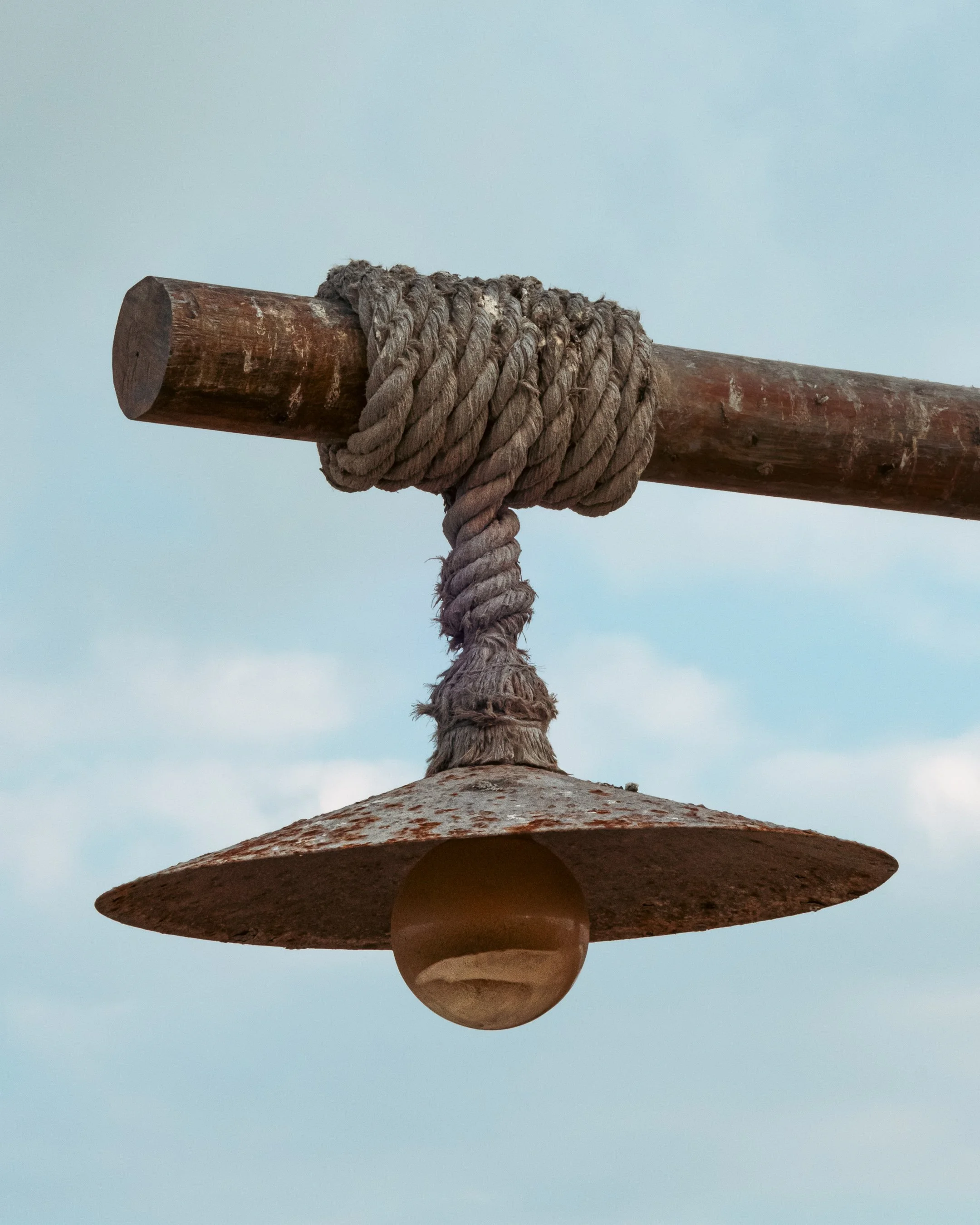Close-up of a wooden Indian club balance with a rope tied around its handle, against a pale sky background.
