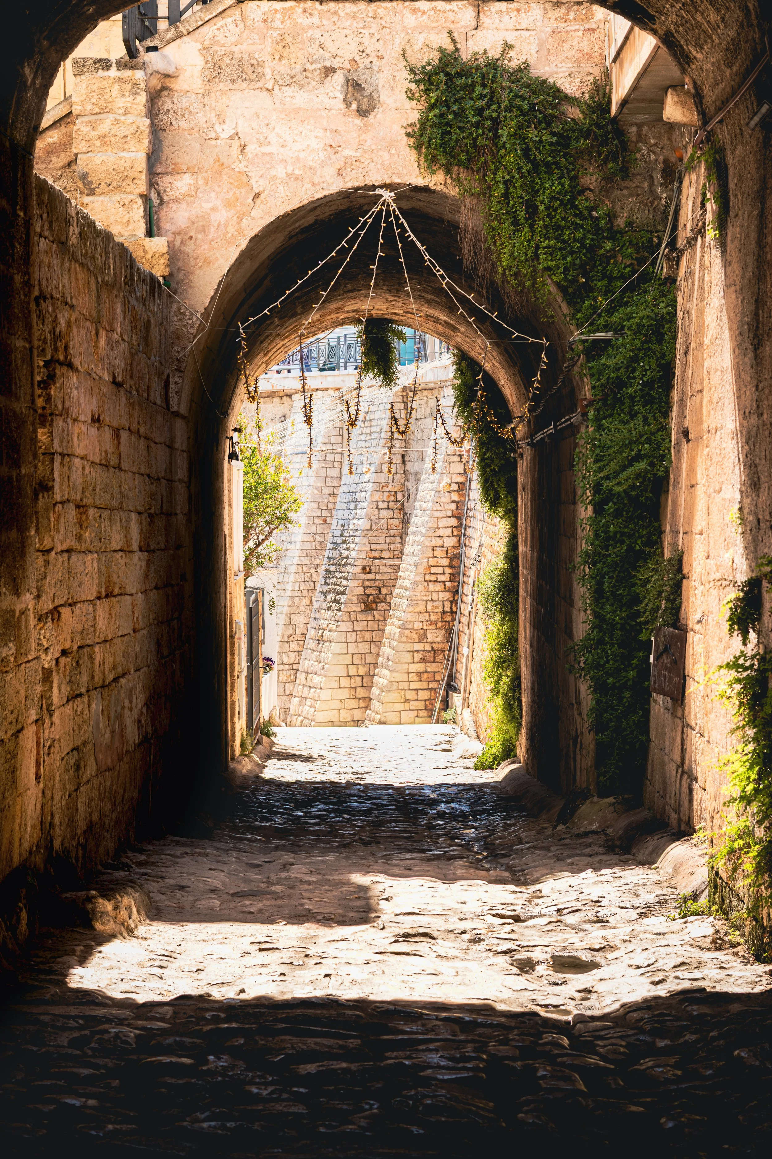 A stone archway in a narrow alley with cobblestone pavement in Puglia, Italy.