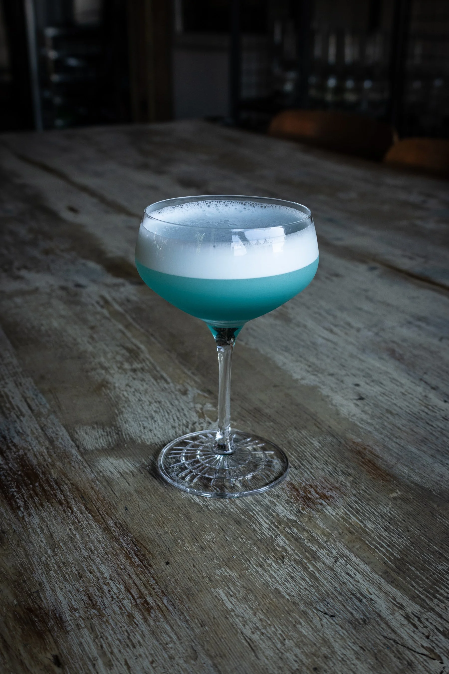 A blue sour cocktail, sat on a textured wooden table. Shot for a cocktail bar in the heart of Auckland.