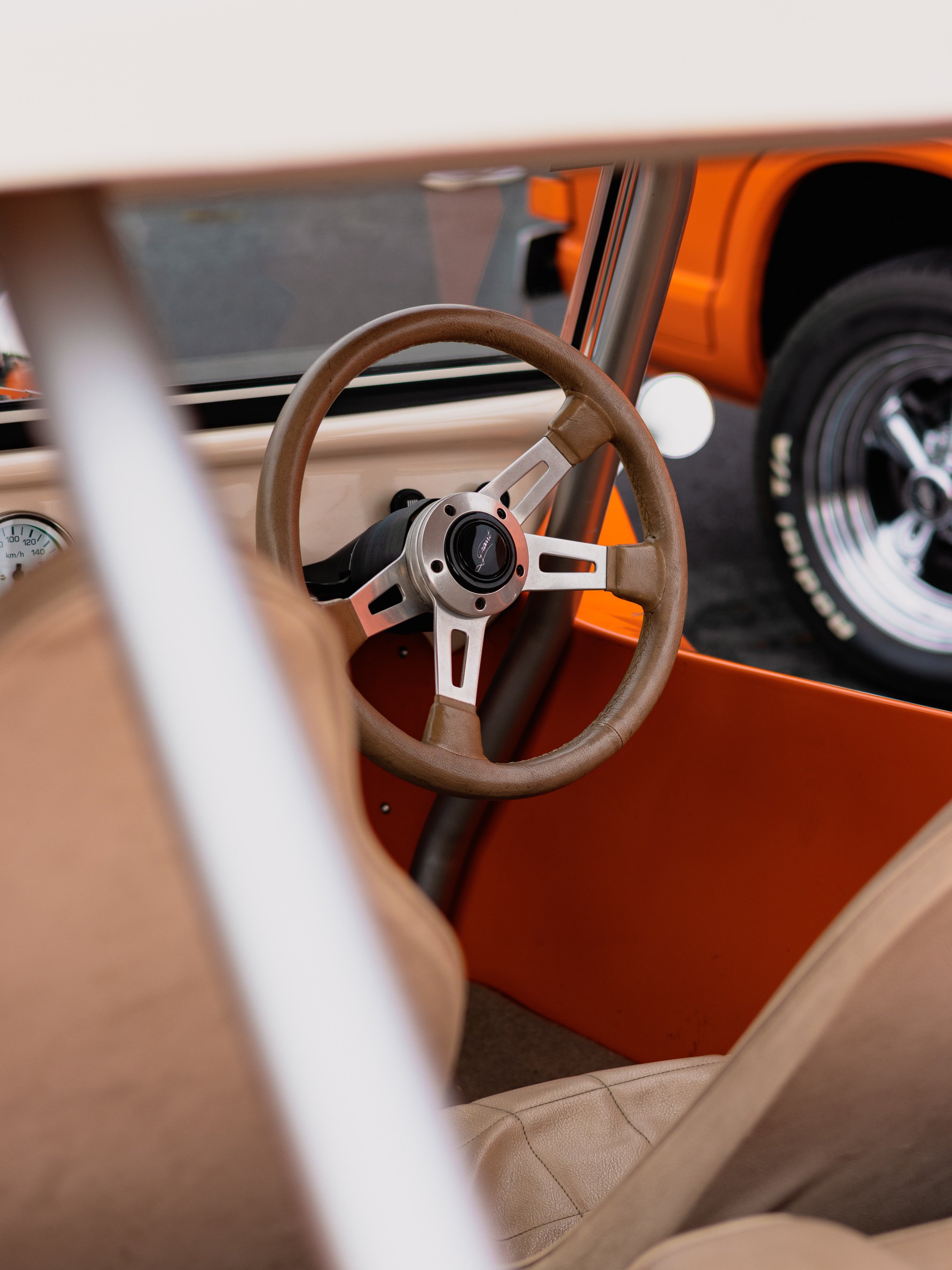 View of a vintage cream-colored car interior, against a white dashboard with orange accents.