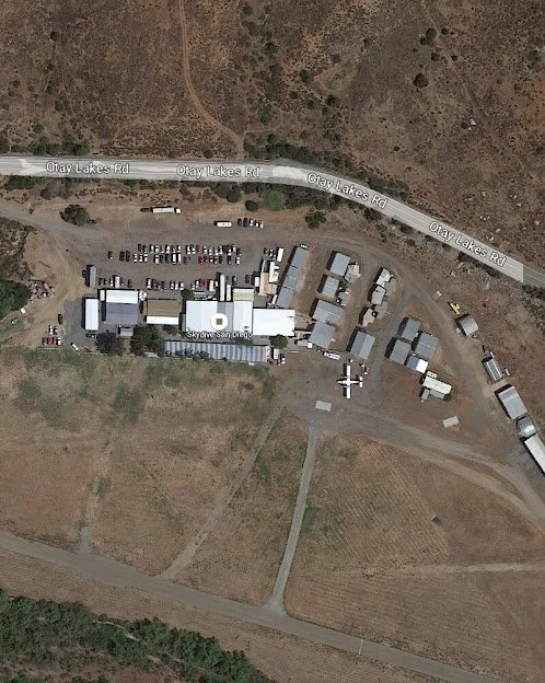 Aerial view of a property next to Otay Lakes Road with multiple buildings, vehicles, and open fields.