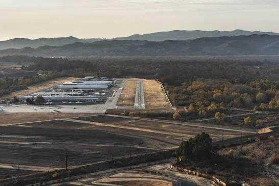 Aerial view of a large landscape with rail tracks, open land, and industrial buildings, with mountains in the background.