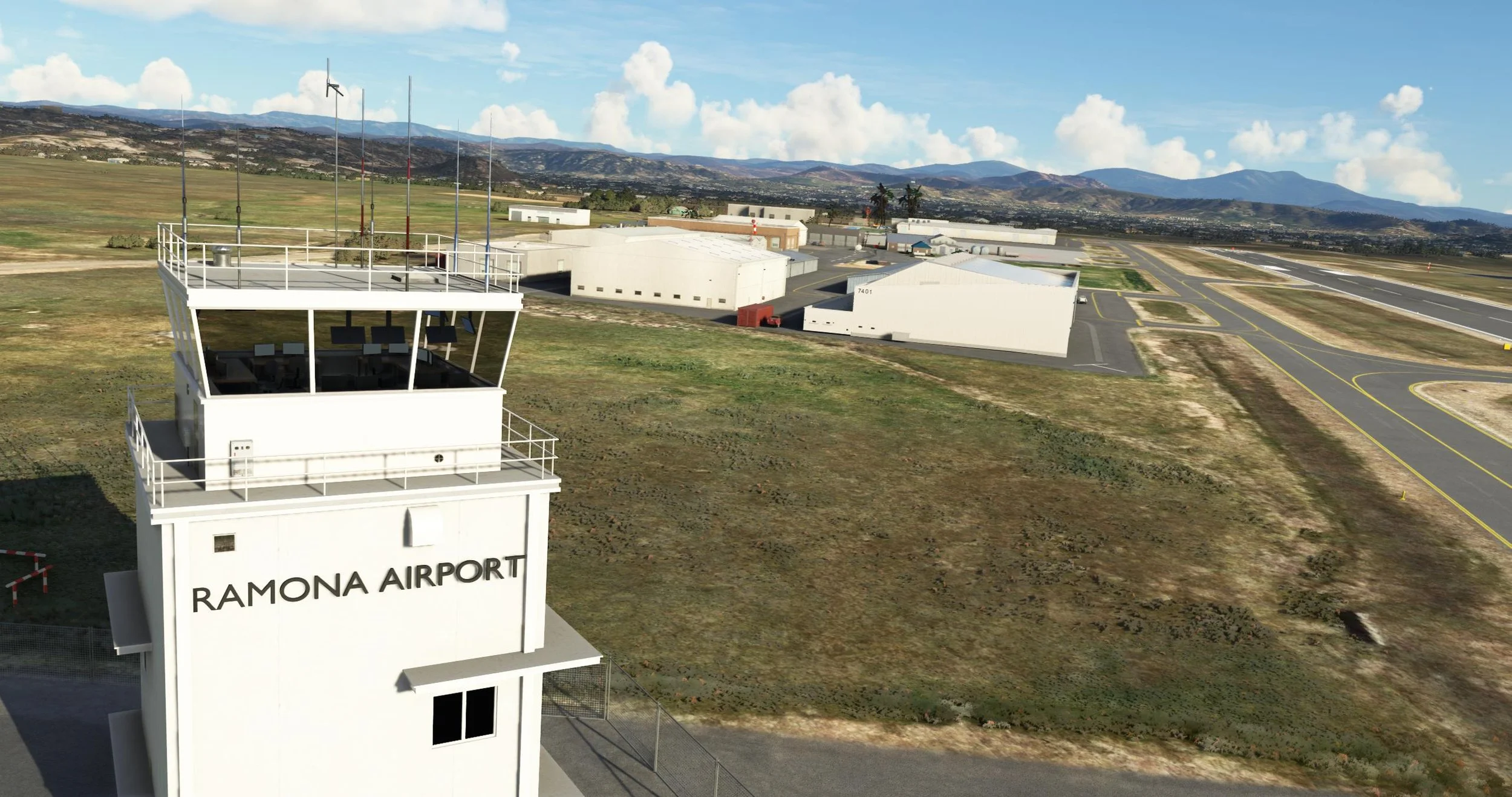 Overview of Ramona Airport with the control tower labeled in the foreground. Buildings, runways, and taxiways extend into the distance with mountains in the background and partly cloudy skies.