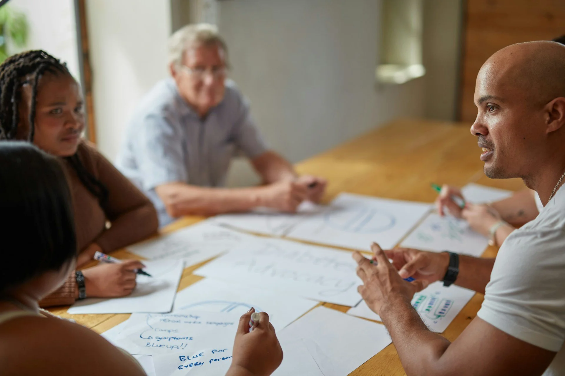 A group of people sitting around a table engaged in a brainstorming session, with papers and markers in front of them.