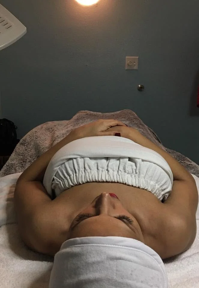 A woman lying down on a massage table with a white towel wrapped around her head, receiving a massage or treatment in a spa or wellness setting.