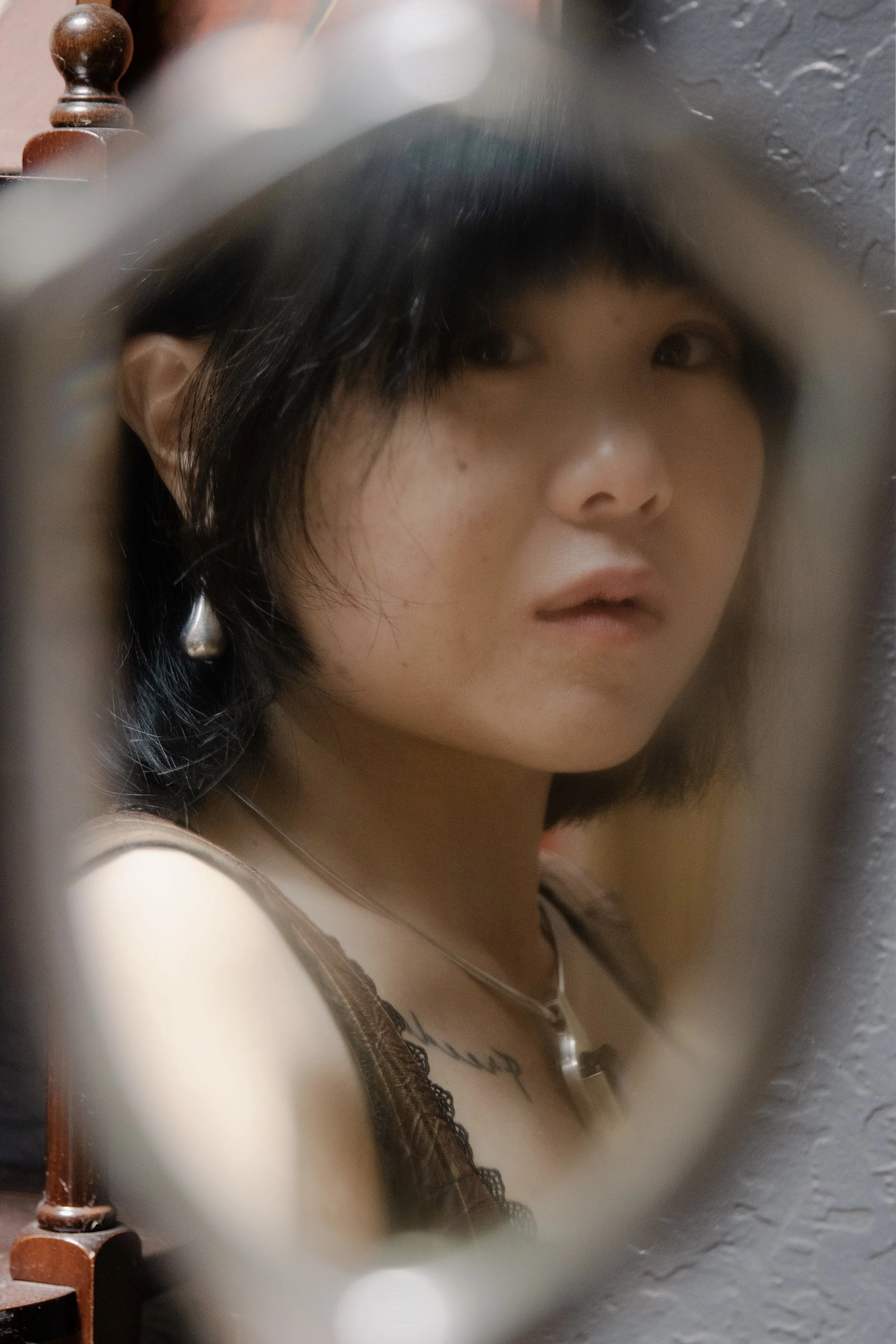 A woman with dark hair and an earring, looking to the side, wearing a black lace top, seen through an uncertain viewing angle.