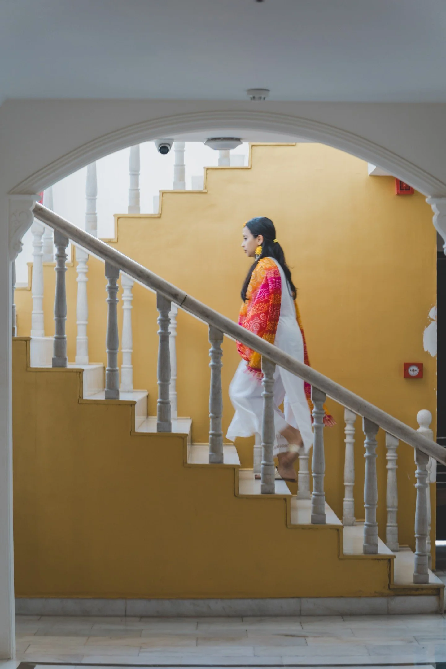 Person walking down a staircase with white railings and a yellow wall background.