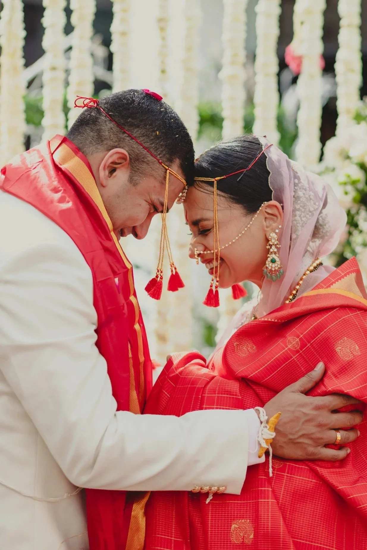 A couple dressed in traditional Indian wedding attire engaging in a forehead touch during their wedding ceremony.