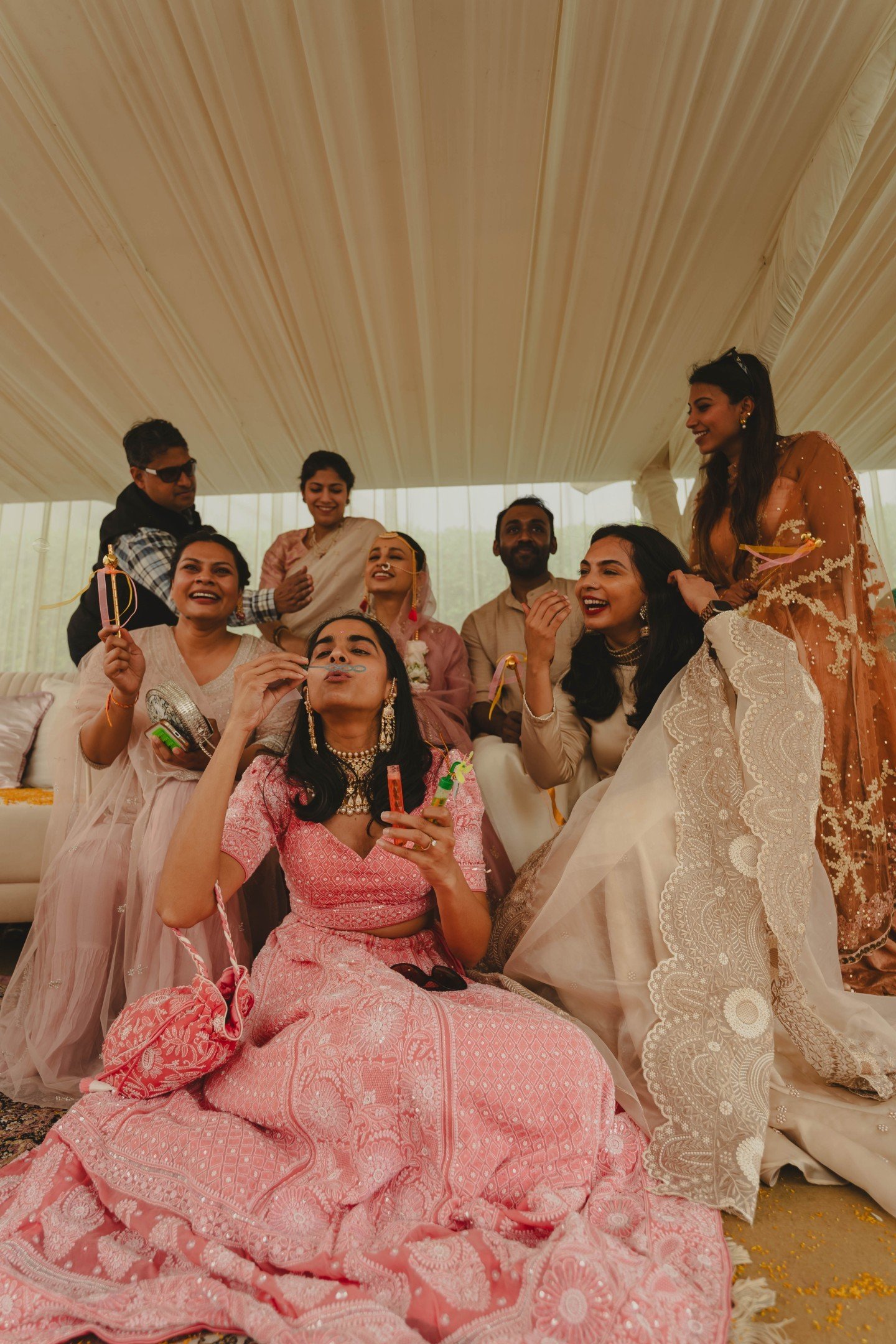 Group of people dressed in traditional Indian attire, celebrating, smiling, with some holding sparklers, in a decorated indoor setting.