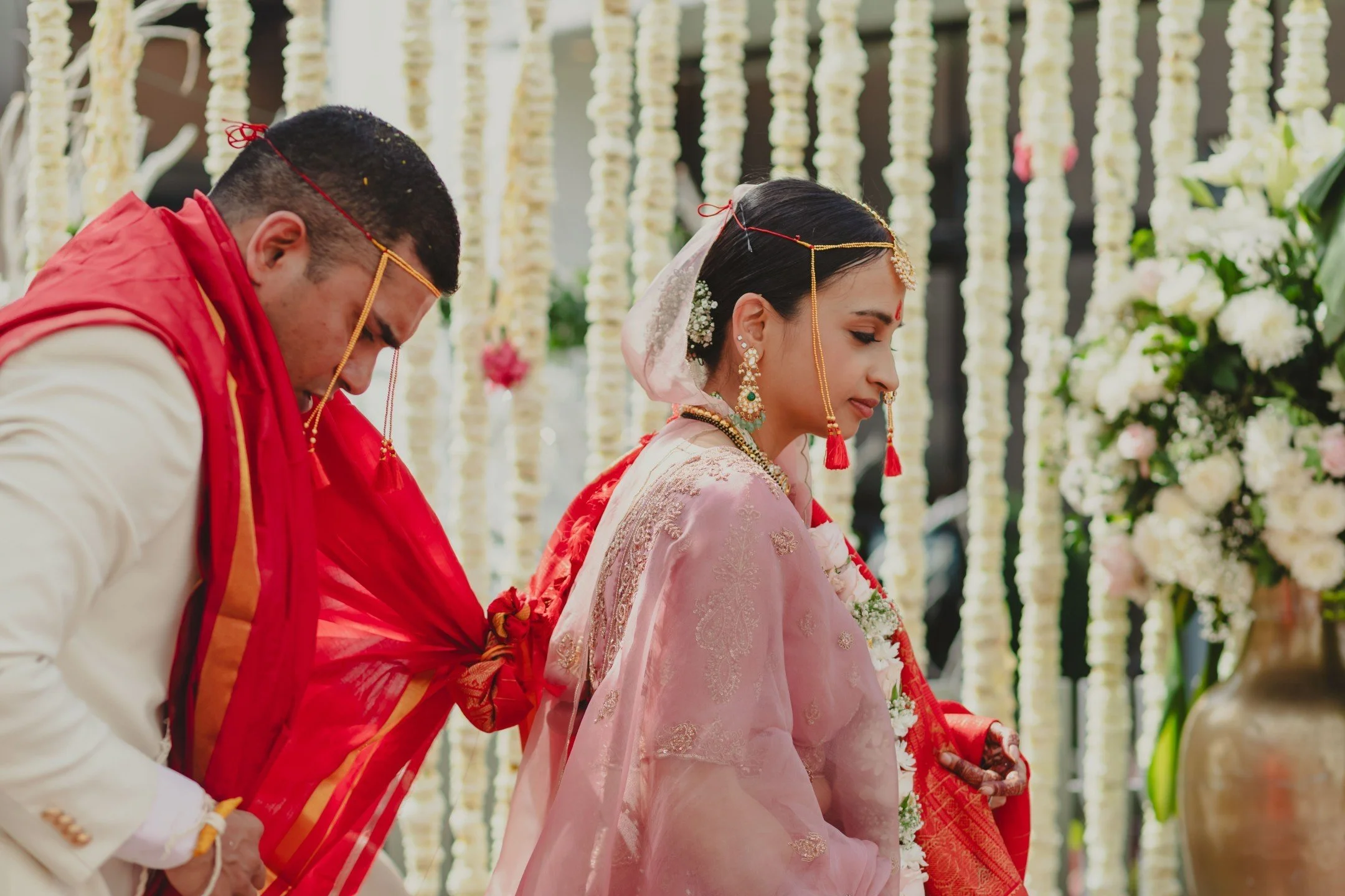 Indian wedding ceremony with bride and groom standing with heads bowed, decorated with flowers.