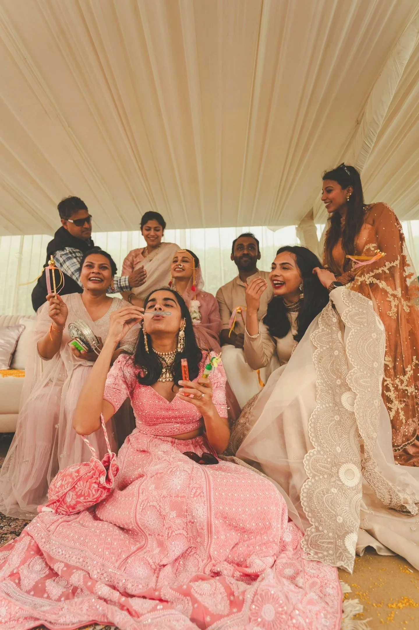 Group of people celebrating Indian wedding, some dressed in traditional attire, under a decorated tent.