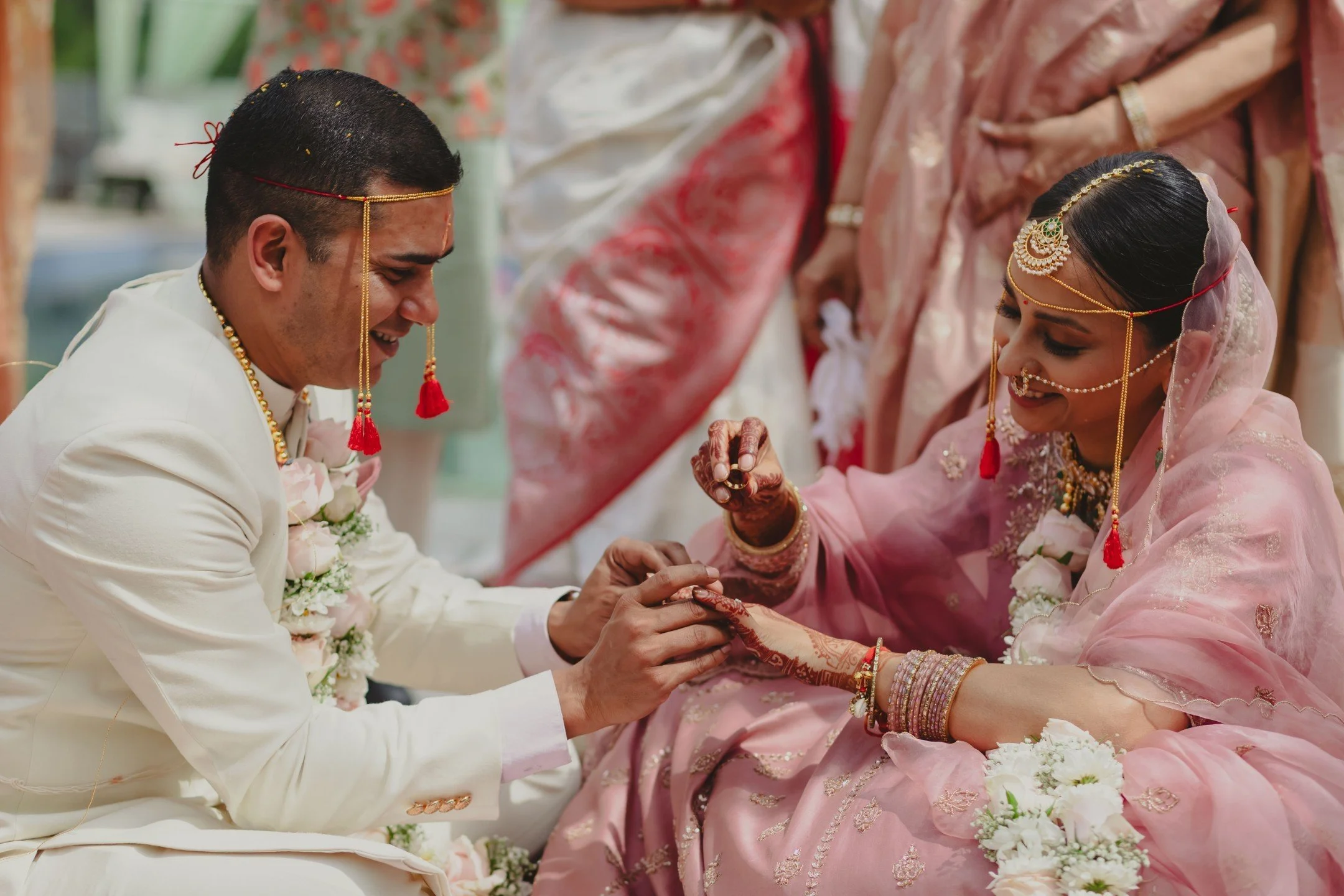 An Indian bride and groom during a wedding ceremony, wearing traditional attire and jewelry, exchanging rings.