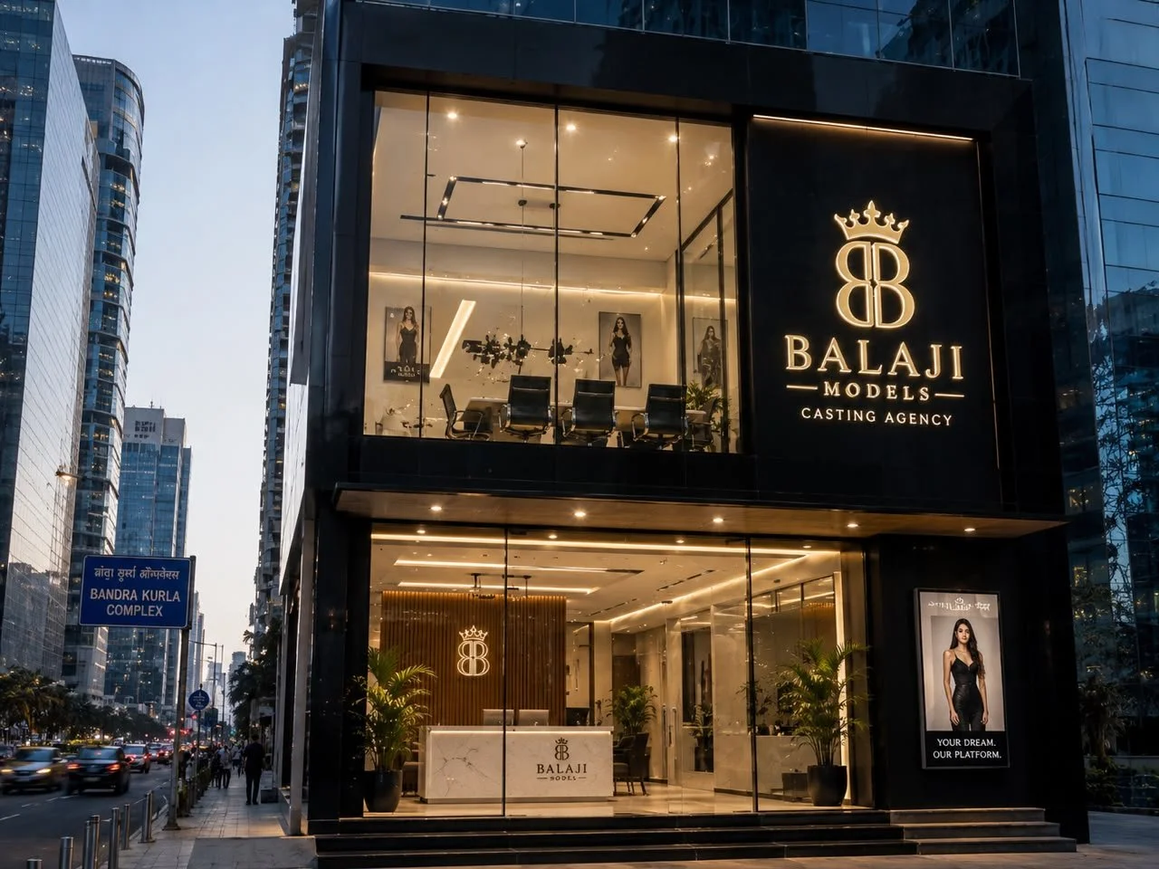 The exterior of a modern, multi-story building with large glass windows, houses the Balaji Models casting agency. The business signs and logos are illuminated, with a prominent sign displaying a crown above a stylized 'B'. Inside, the interior features a reception area with a counter, potted plants, and photographs of models on the walls.