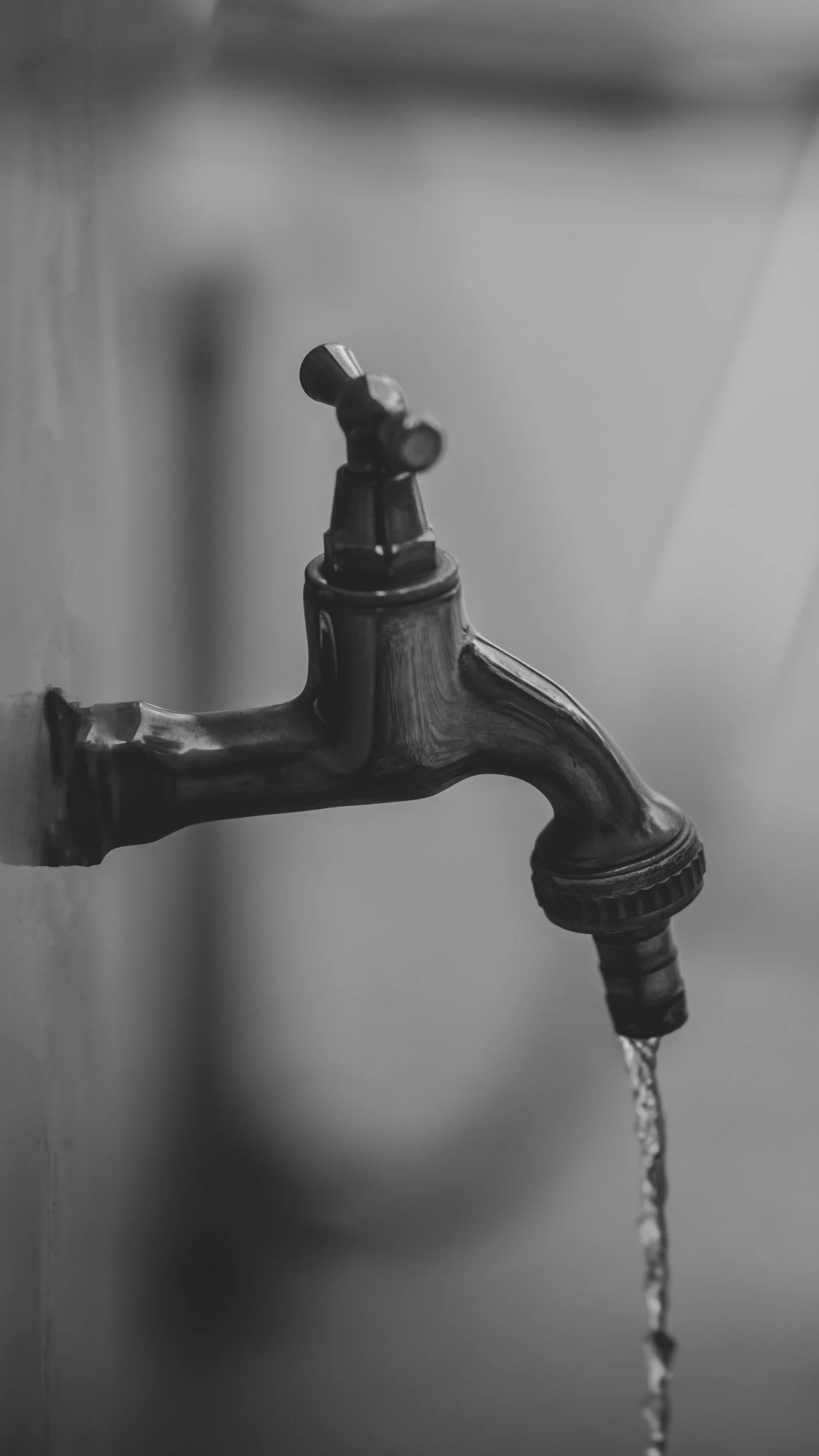 A black and white photo of a traditional outdoor tap with water leaking from it.