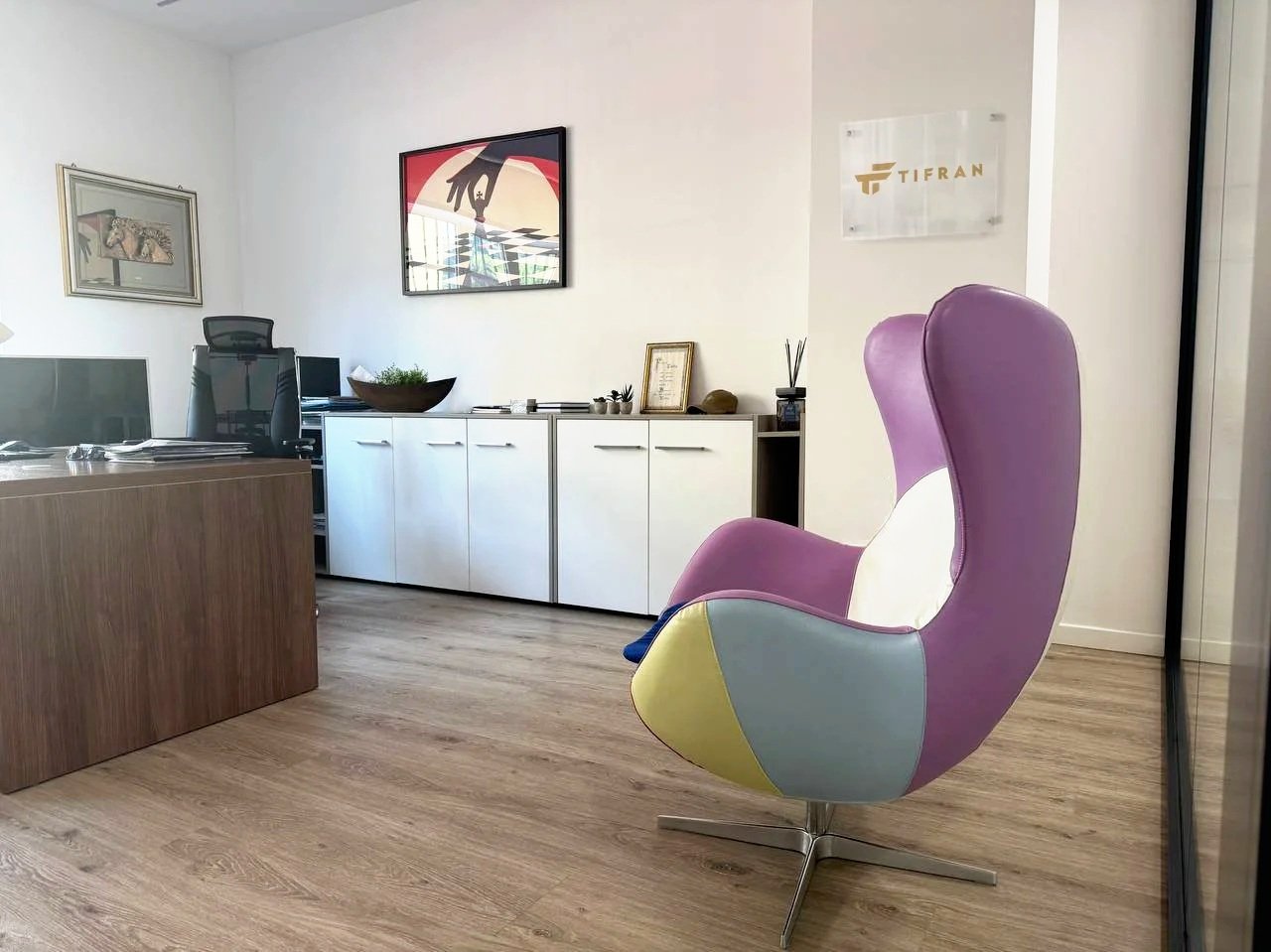 Studio con scrivania, sedie colorate, quadri alle pareti e arredo moderno.