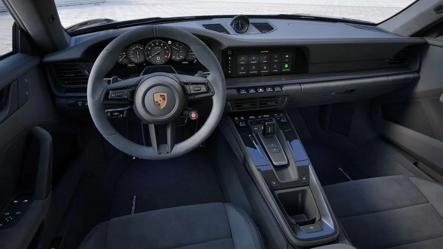 Interno di un'auto sportiva Porsche con volante, pannello di controllo digitale e cambio automatico.