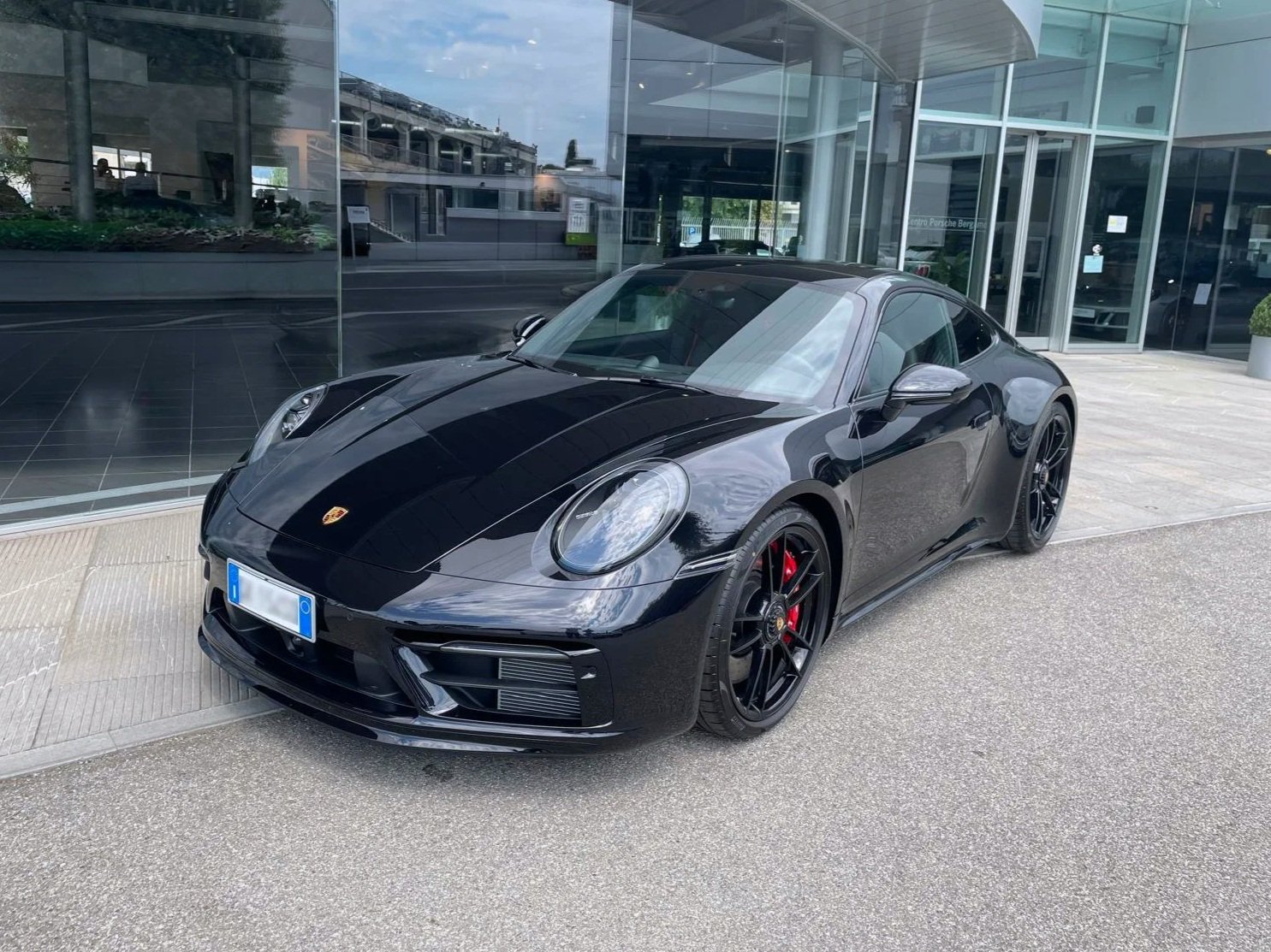 Auto sportiva Porsche 911 bianca con tetto maxi in nero parcheggiata su strada in ambiente urbano.