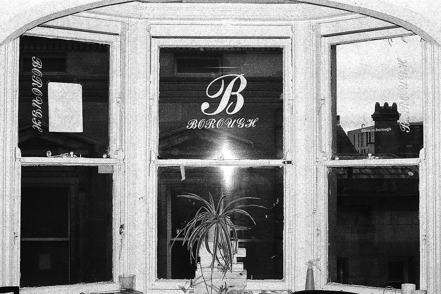 Interior view of front windows with 'Borough' signage and a potted plant on the window sill, black and white photograph.