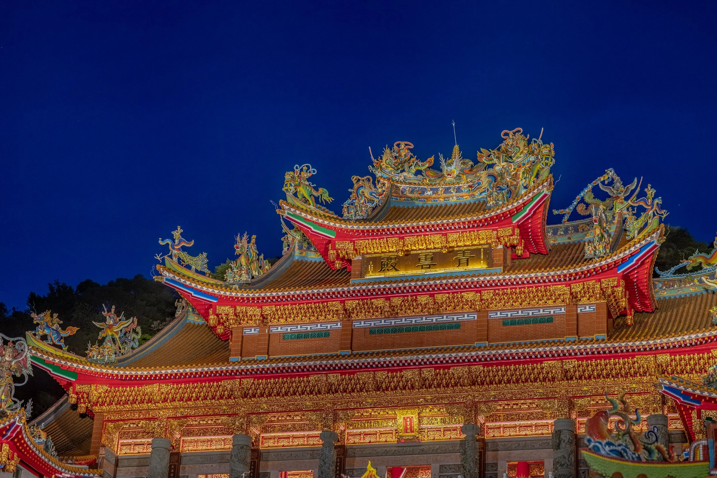 A traditional Chinese temple with ornate golden and multicolored decorations, dragons on the roof, and a deep blue night sky in the background.