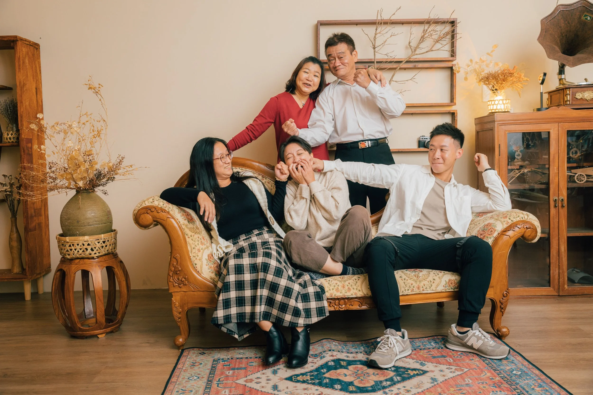 A multigenerational Asian family of six sitting and standing in a living room, celebrating with smiles and gestures.