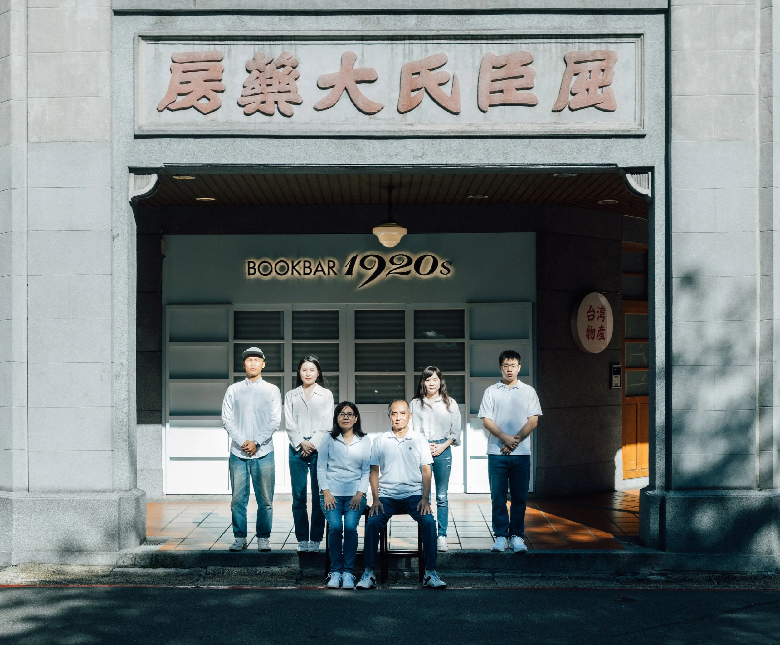 group of nine people posing in front of building with Chinese characters and a sign reading 'Bookbar 1920s' on the entrance.