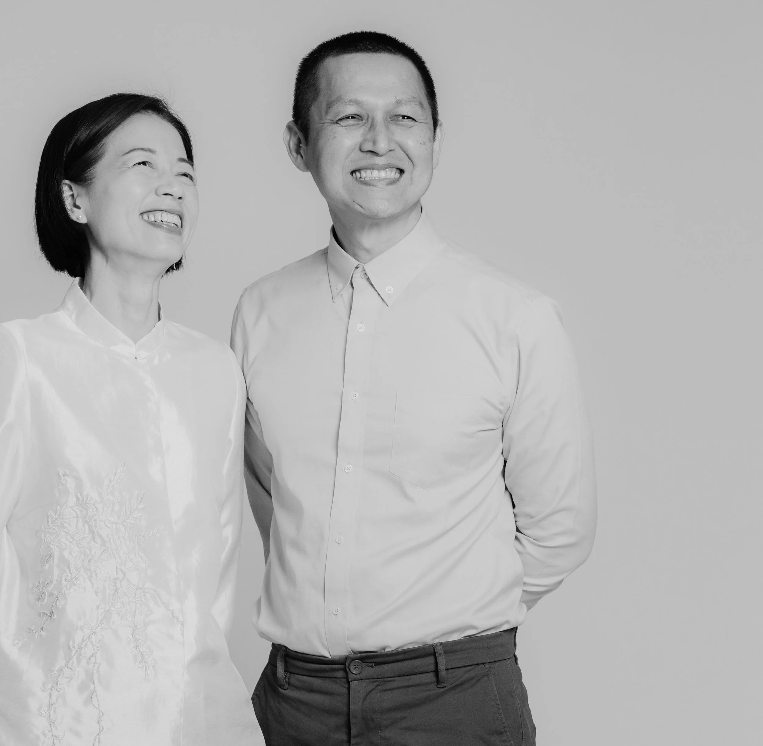 Black and white photo of a young woman and a young man smiling, standing next to each other against a plain background, wearing collared shirts.