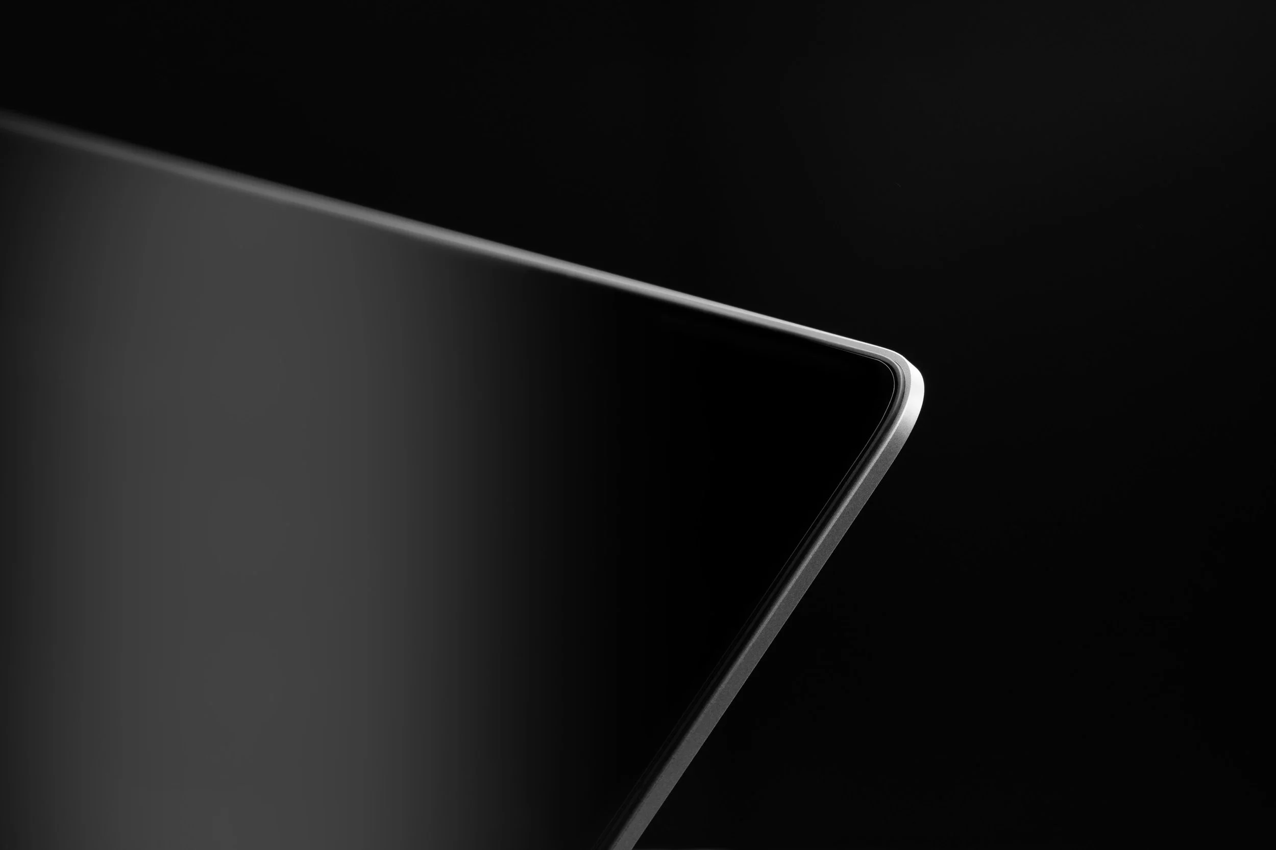 Close-up of a sleek, black electronic device with curved edges and a reflective surface, partially visible against a dark background.