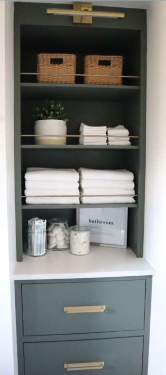 Bathroom storage cabinet with wicker baskets, potted plant, folded towels, toothbrushes, cotton balls, and a sign labeled 'bathroom'.