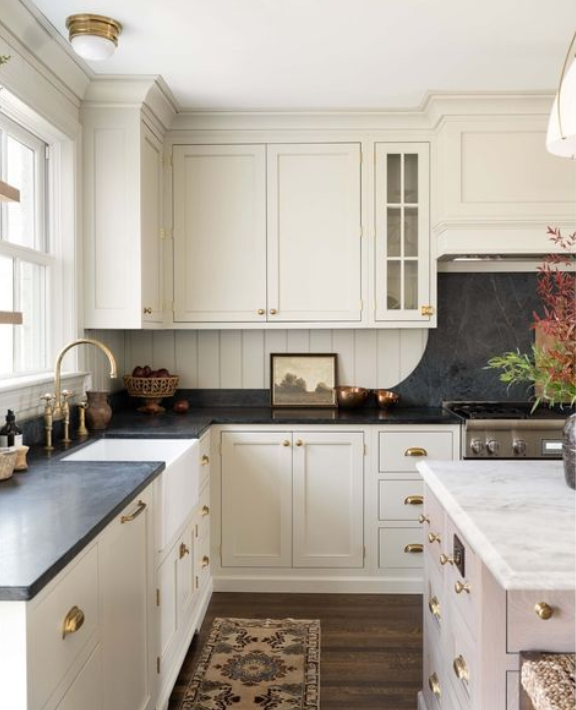 White kitchen with black countertops, brass hardware, a small island, and a window with natural light.