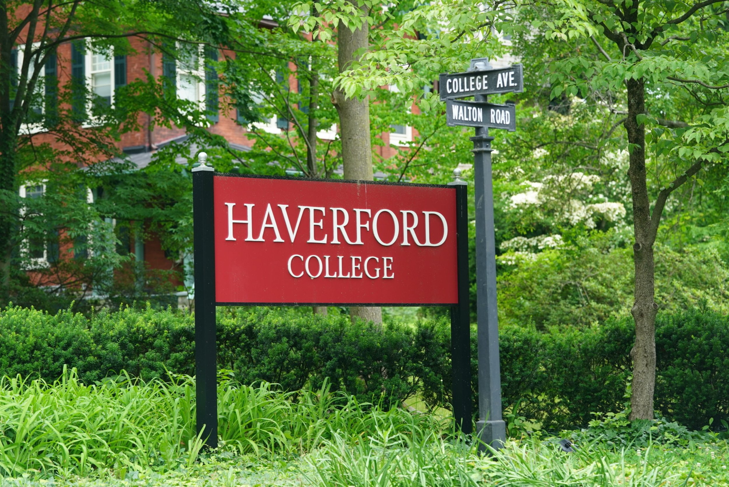 Street sign at the corner of College Avenue and Walton Road in front of a red brick building surrounded by green trees and shrubs.