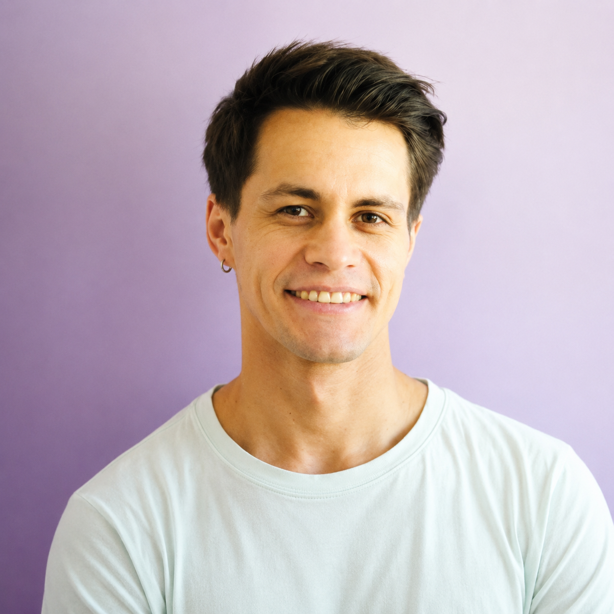 Young man with short dark hair, wearing a white T-shirt and a small hoop earring, smiling against a purple background.