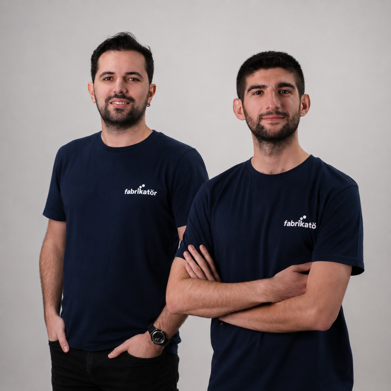 Two young men wearing matching navy blue T-shirts with 'fabrikato' logo standing against a plain light gray background.