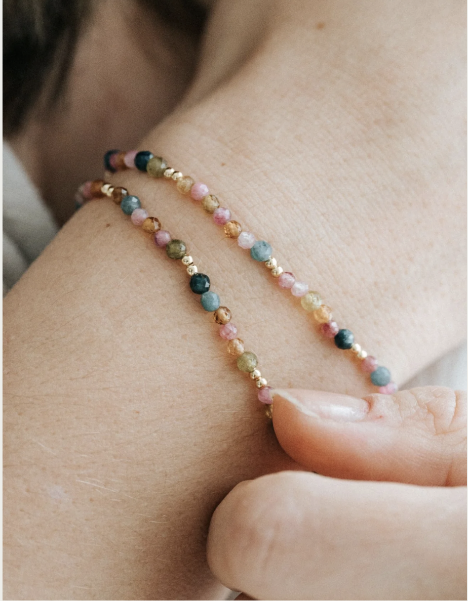 Nahaufnahme eines Handgelenks mit einem zarten, mehrfarbigen Perlenarmband.
