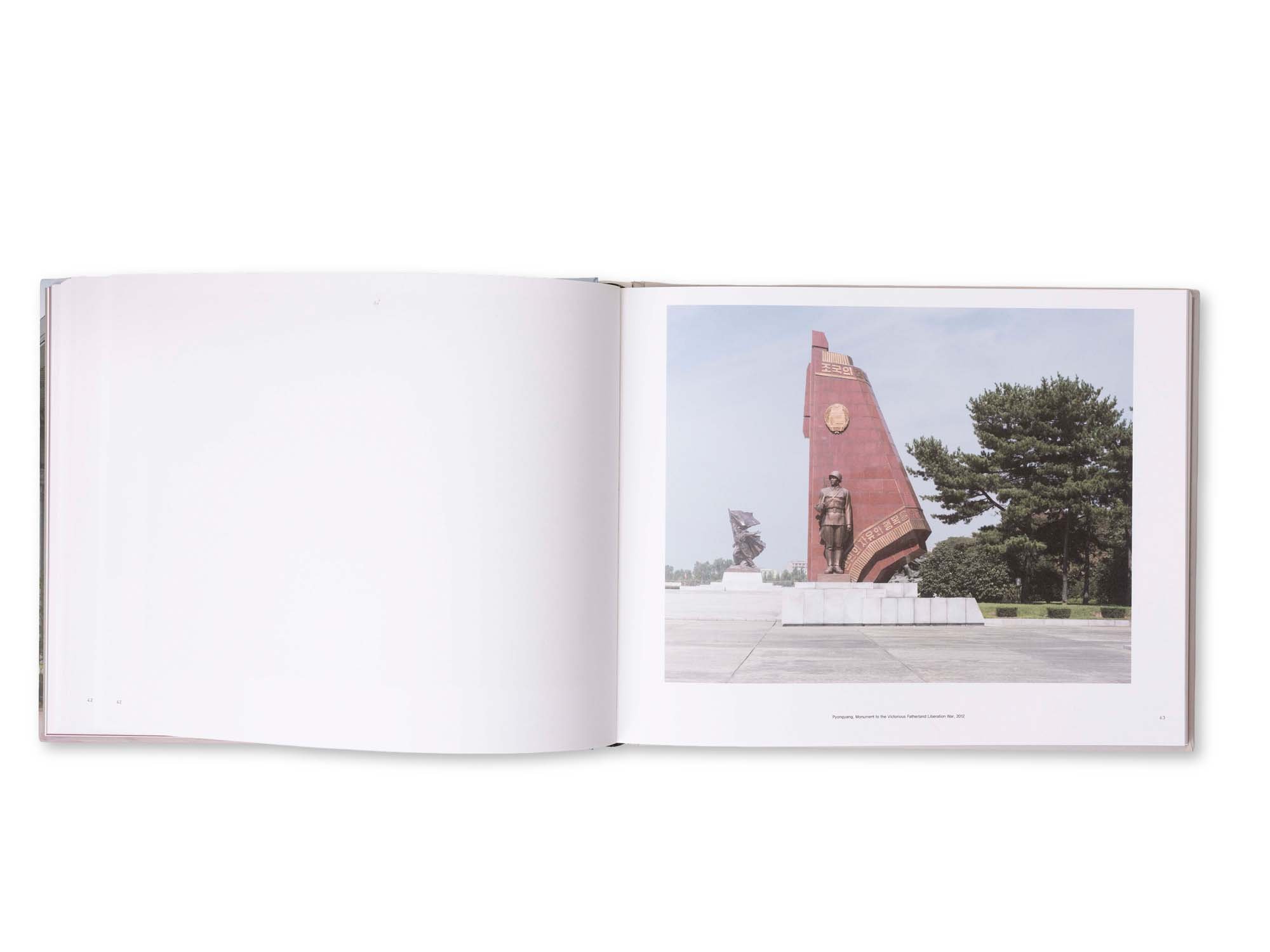 Offenes Buch mit einer Fotoseite eines Denkmals in Pyongyang, Nordkorea, bestehend aus einem großen roten Obelisken mit Statuen und Bäumen im Hintergrund.