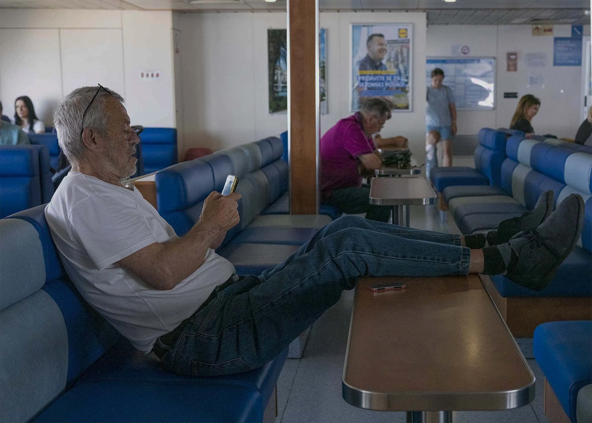 Commuters on the early morning ferry from Split to Brač, Croatia, resting and using smartphones on the deck, documentary photography by Roman Bezjak