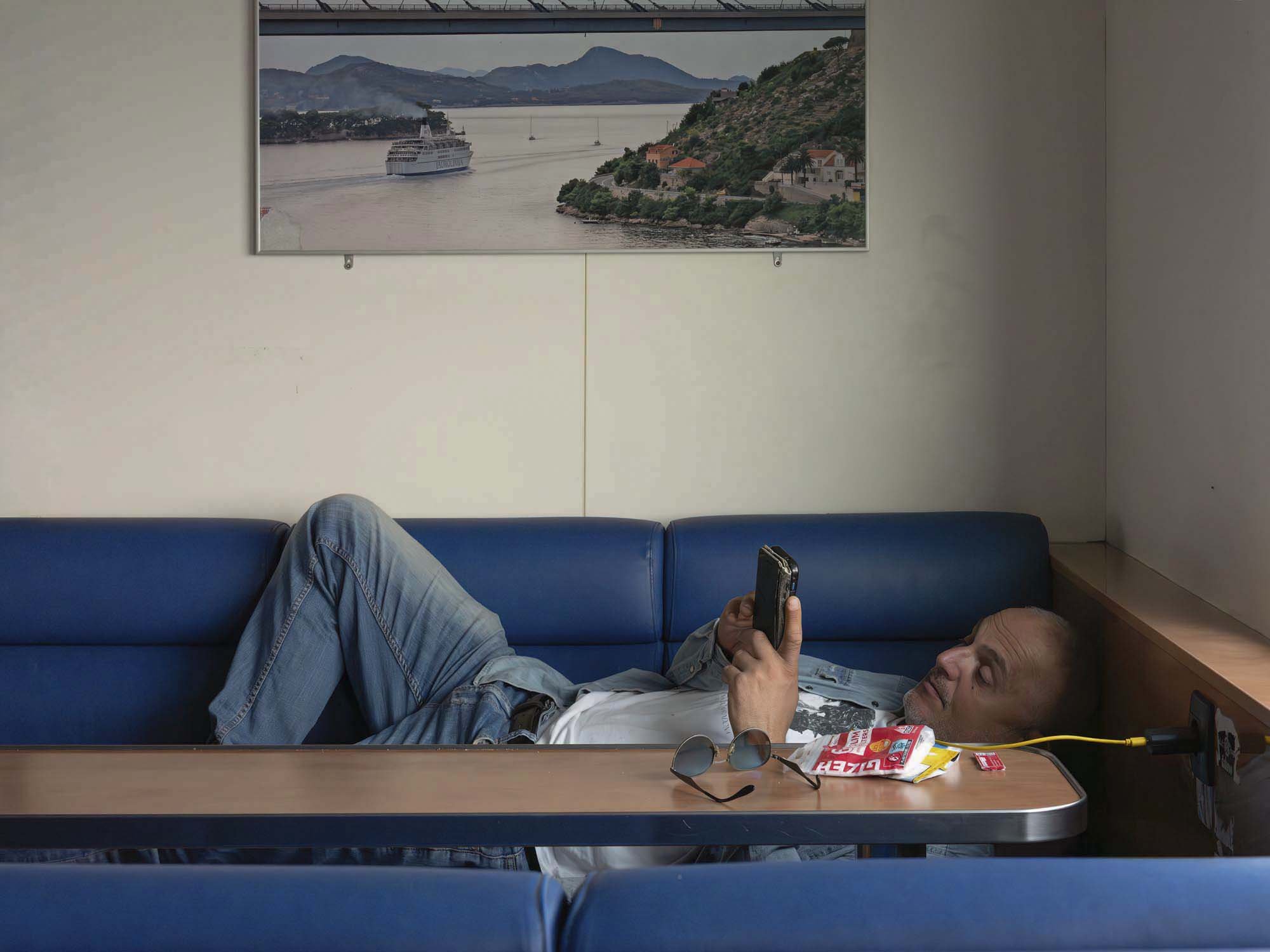 Commuters on the early morning ferry from Split to Brač, Croatia, resting and using smartphones on the deck, documentary photography by Roman Bezjak